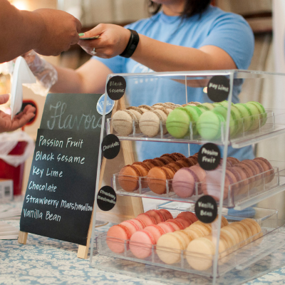 someone handing cash over a till counter with a stand full of macaroons on the side