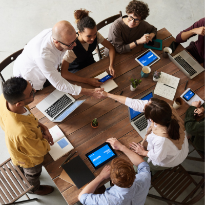 a group of people working and collaborating around a table with two people leaning across to shake hands